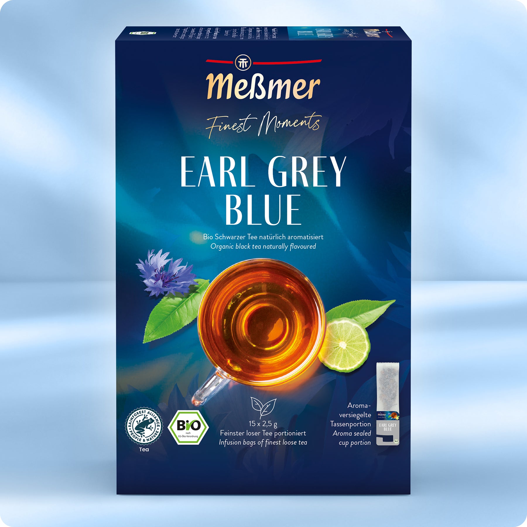 Eine Schachtel Meßmer DE Bio Earl Grey Blue mit einer Teetasse, blauen Blüten, grünen Blättern und Zertifizierungslogos auf blauem Hintergrund. Enthält 15 Bio-Schwarzteebeutel.