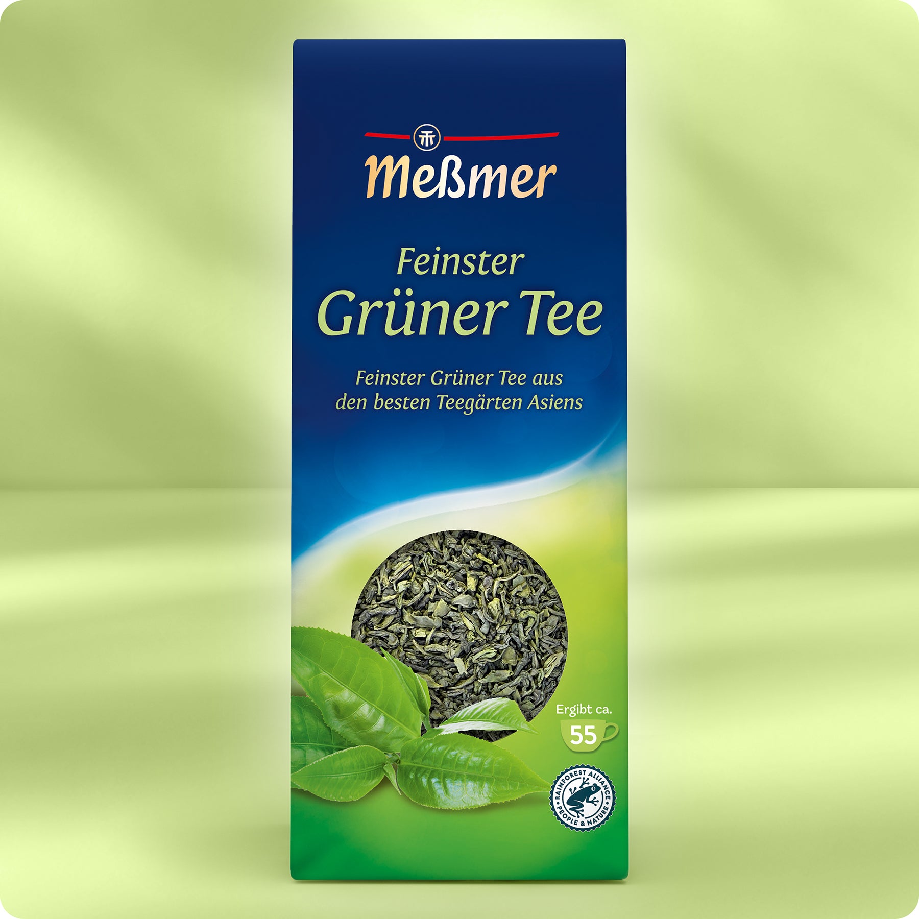 Eine Schachtel Meßmer DE Feinster Grüner Tee mit einem Bild von losen grünen Teeblättern und frischen Teeblättern auf der Vorderseite vor einem grünen Hintergrund.
