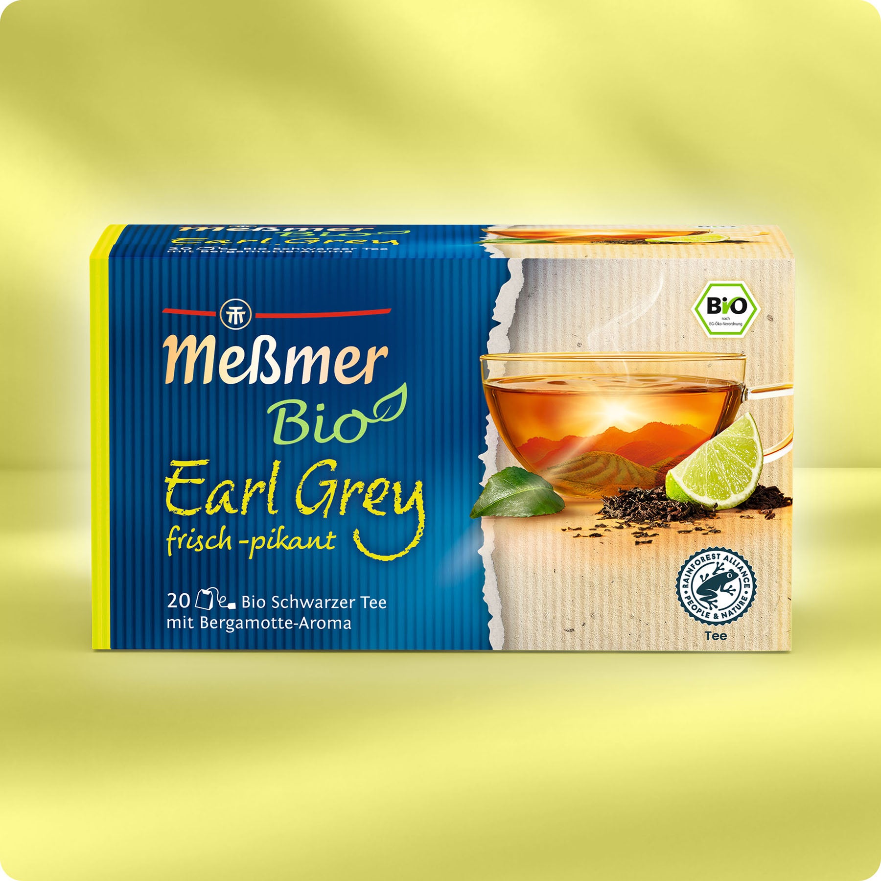 Eine Schachtel Meßmer DE Bio Earl Grey mit einer gläsernen Teetasse, losen Teeblättern, einer Limettenscheibe mit Bergamotte-Note und grünen Blättern auf gelbem Hintergrund. Enthält 20 Bio-zertifizierte Teebeutel.