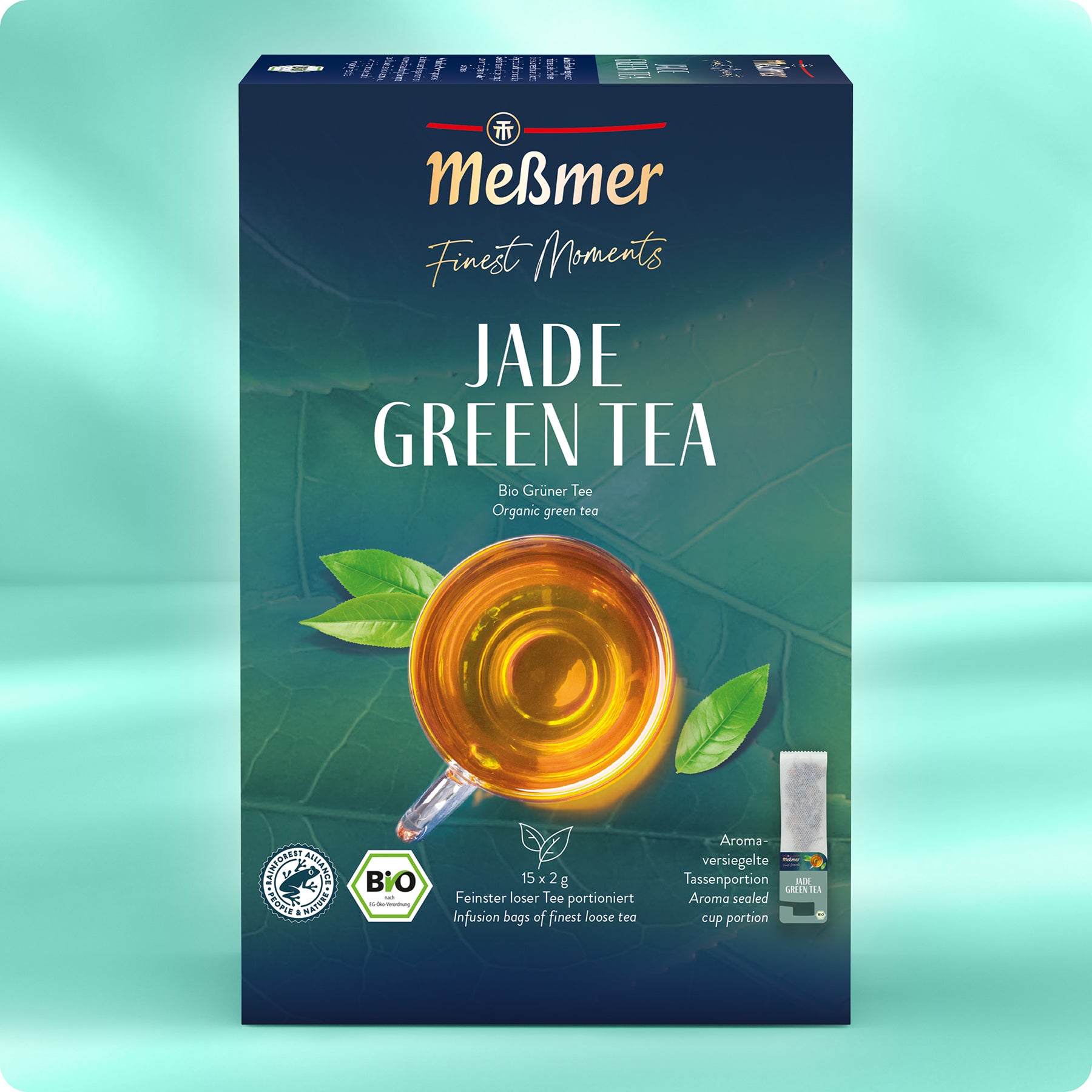 Eine Schachtel Meßmer DE Bio Jade Grüner Tee zeigt eine grüne Verpackung mit goldener und weißer Schrift, eine Tasse Tee und grüne Teeblätter. Die Logos der Bio-Zertifizierung sind enthalten. Entdecken Sie auch Meßmers Earl Grey und Schwarzteesorten.