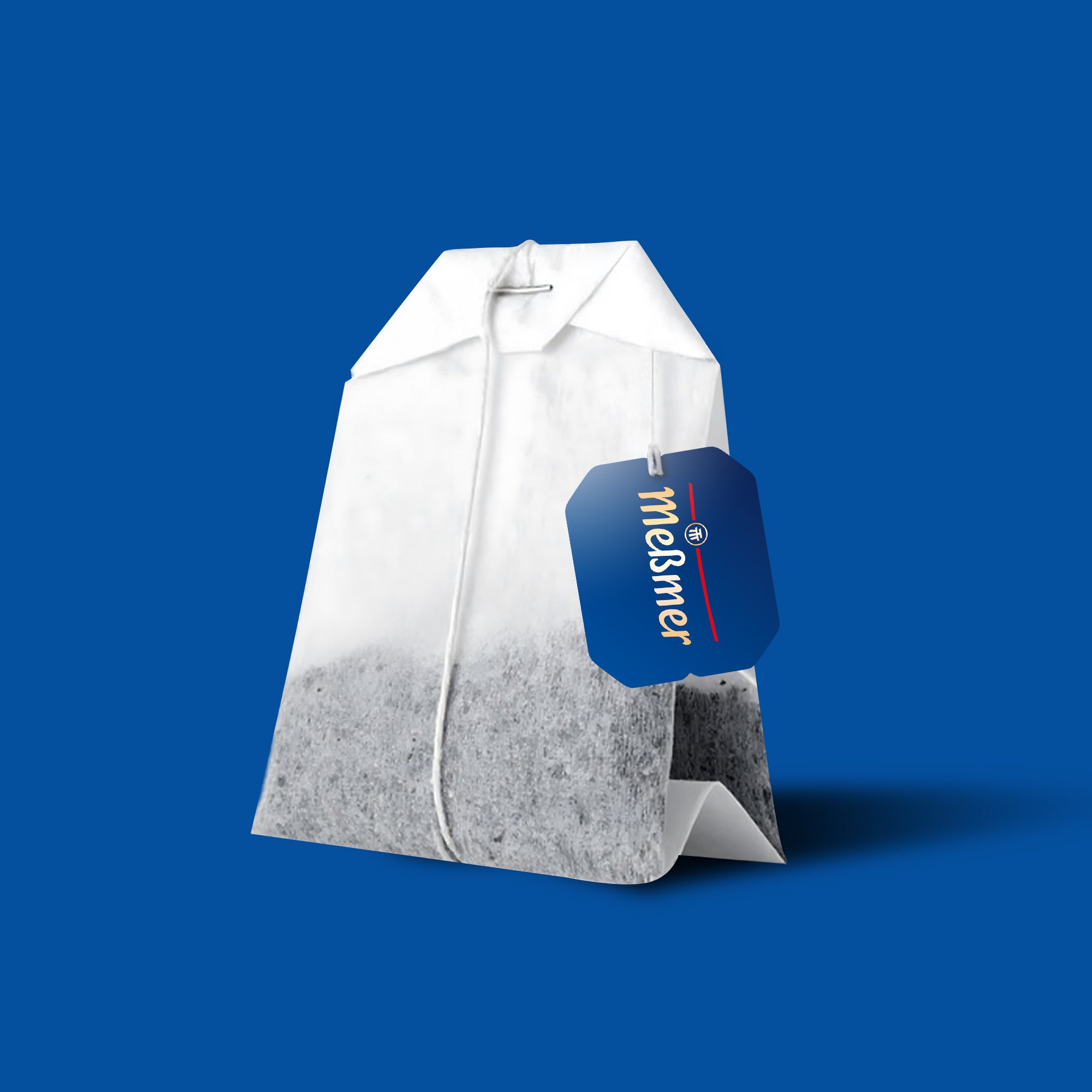Ein einzelner Teebeutel mit einem blauen Etikett mit der Aufschrift "Meßmer" ruht auf einem einfarbig blauen Hintergrund.